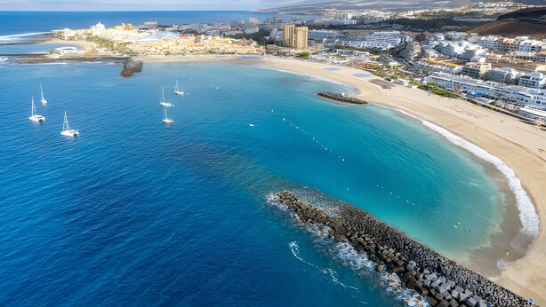 A coastal town with a sandy beach, clear blue waters, and several sailboats.