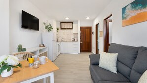 A modern kitchen with white cabinets, a flat-screen TV, and a dining area with a wooden table and chairs.