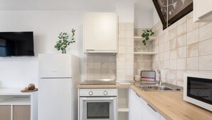 A modern kitchen with white cabinetry, a built-in oven, a microwave, and a television above the counter.