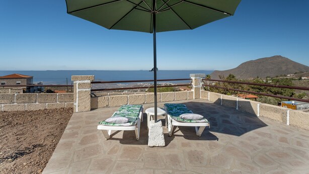 Una terrazza con due poltrone, un ombrellone e vista sul mare e sulle montagne.