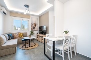 A modern living room with a sofa, a dining table with chairs, a TV, and a ceiling light fixture.
