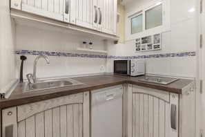 Une cuisine avec des meubles blancs en bois, un évier en acier inoxydable, un four à micro-ondes et un lave-vaisselle.