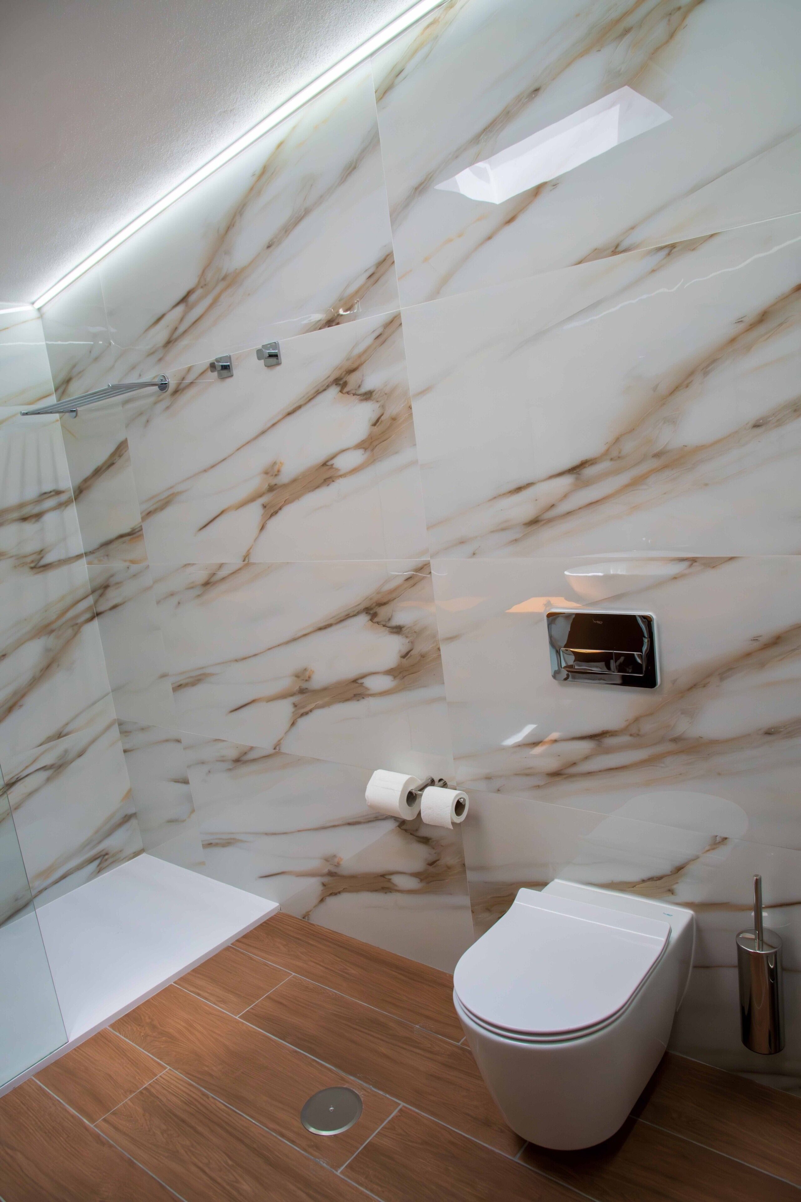 Een moderne badkamer met een marmeren wand, een toilet, een douche en een toiletrolhouder.