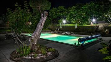Una piscina con sillas de descanso, un árbol y un muro de piedra.
