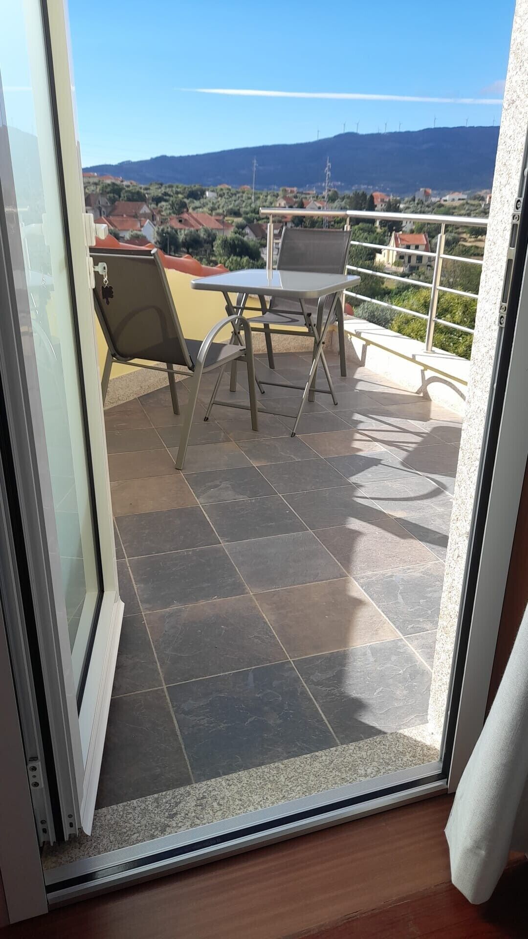 Uma varanda com mesa e cadeiras, vista para o campo e céu claro.