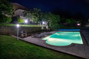 A swimming pool with a stone border, surrounded by a patio area with lounge chairs and umbrellas.