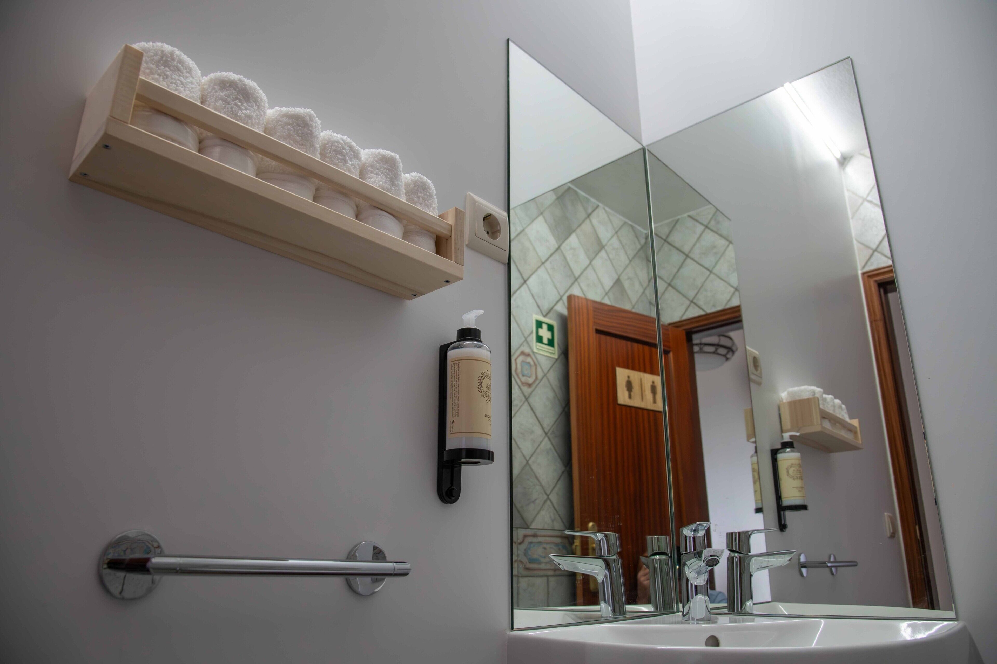 A bathroom with a large mirror, a towel rack with towels, a soap dispenser, and a handrail.