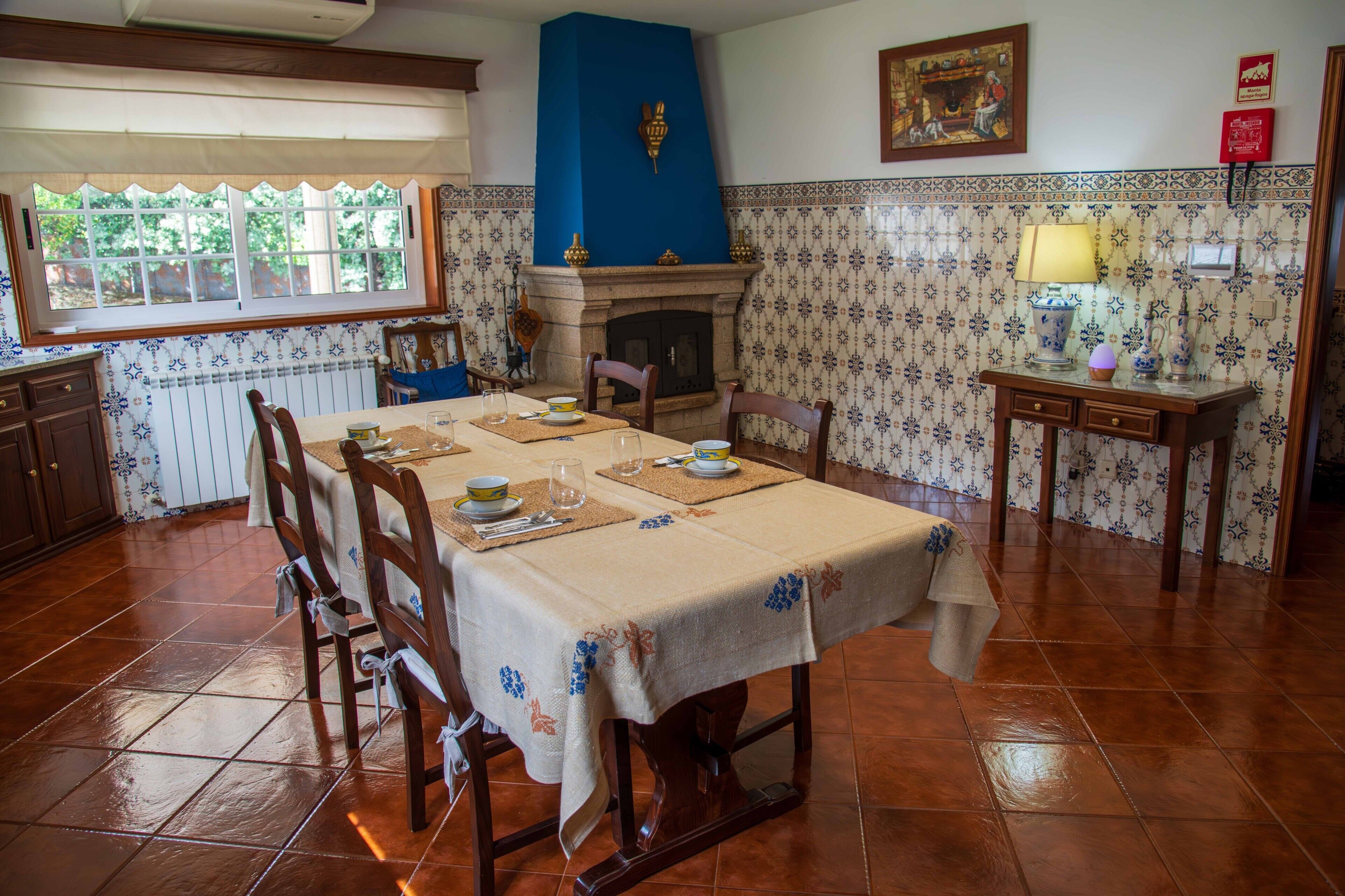 Une salle à manger avec une table dressée pour quatre personnes, une cheminée et un papier peint à motifs.