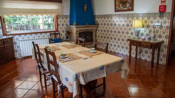 Une salle à manger avec une table dressée pour quatre personnes, une cheminée et un papier peint à motifs.
