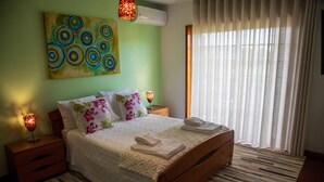 Una cama bien hecha con edredón blanco y almohadas, un cabecero de madera, una lámpara de noche y un cuadro en la pared.