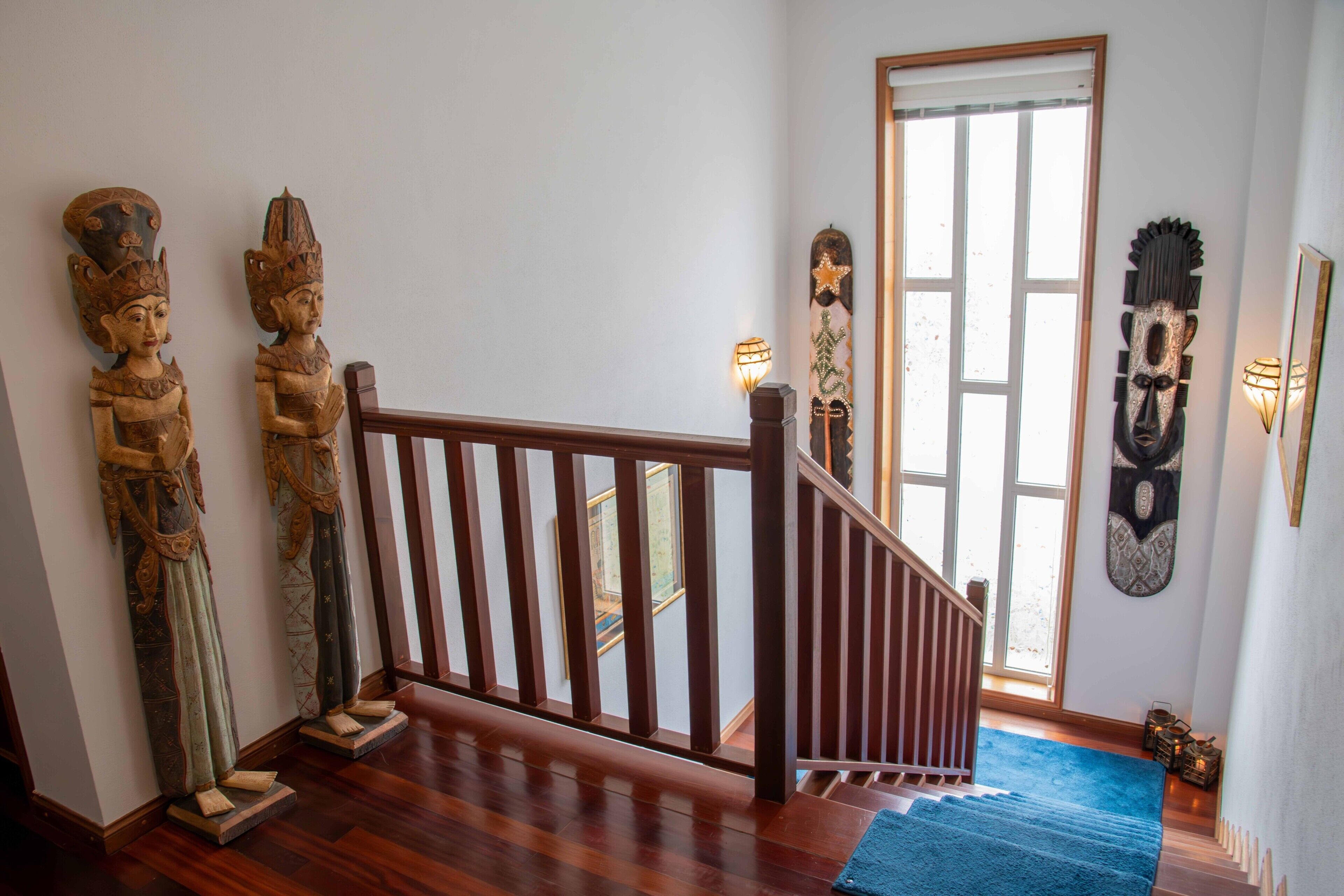 Un escalier avec des rampes en bois, une moquette bleue et des sculptures traditionnelles en bois accrochées au mur.