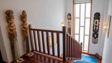 Un escalier avec des rampes en bois, une moquette bleue et des sculptures traditionnelles en bois accrochées au mur.