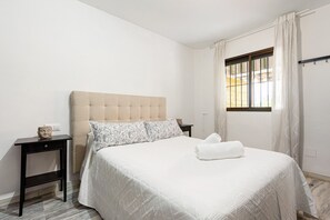 Un lit avec une tête de lit, une table de chevet, une fenêtre avec des rideaux et une serviette sur le lit.