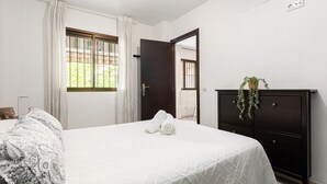 Une chambre à coucher avec un lit, une commode, une fenêtre avec des rideaux et une plante en pot.