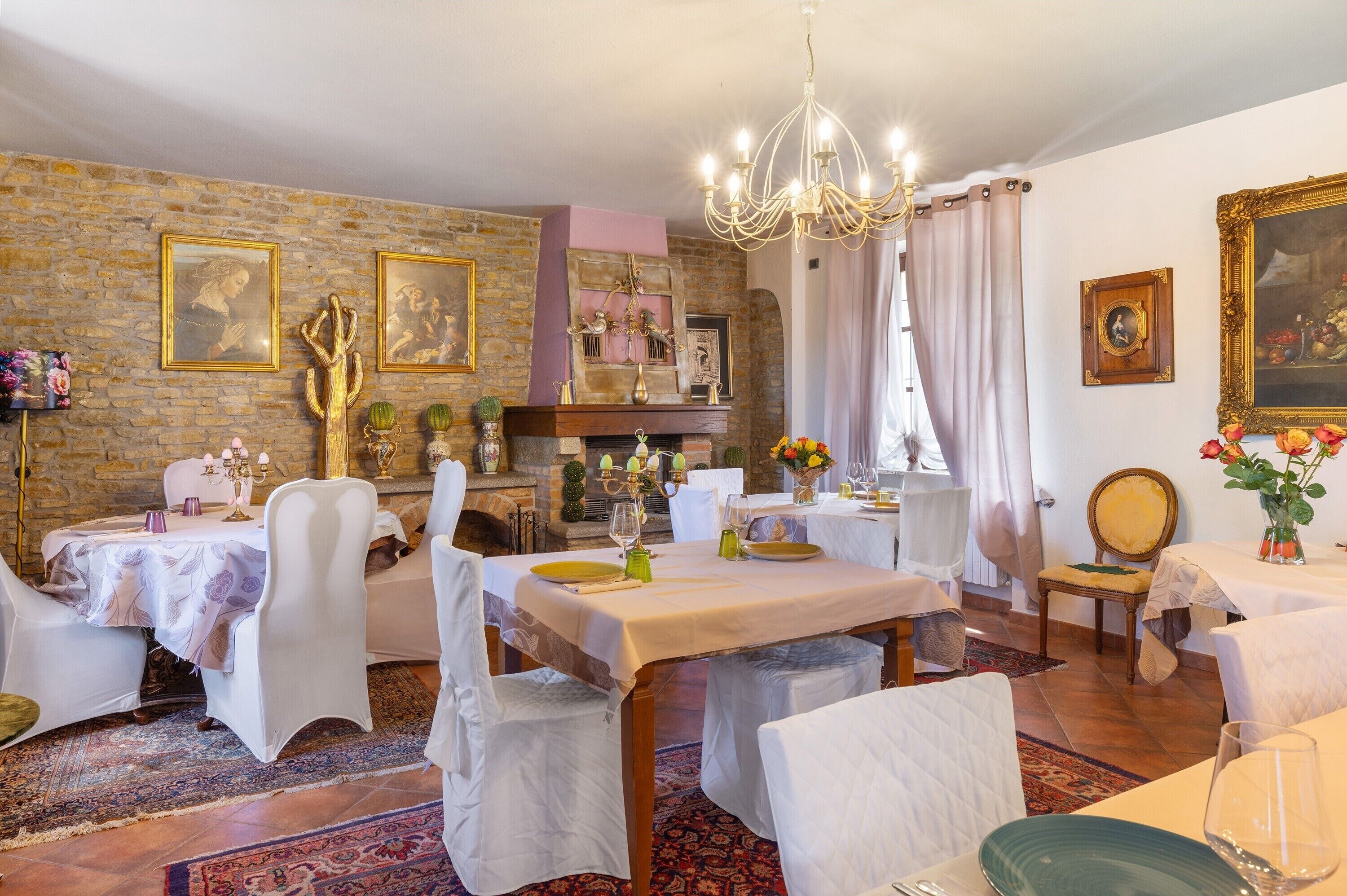 A dining room with a fireplace, chandeliers, and framed artwork on the walls.