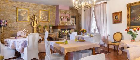A dining room with a fireplace, chandeliers, and framed artwork on the walls.