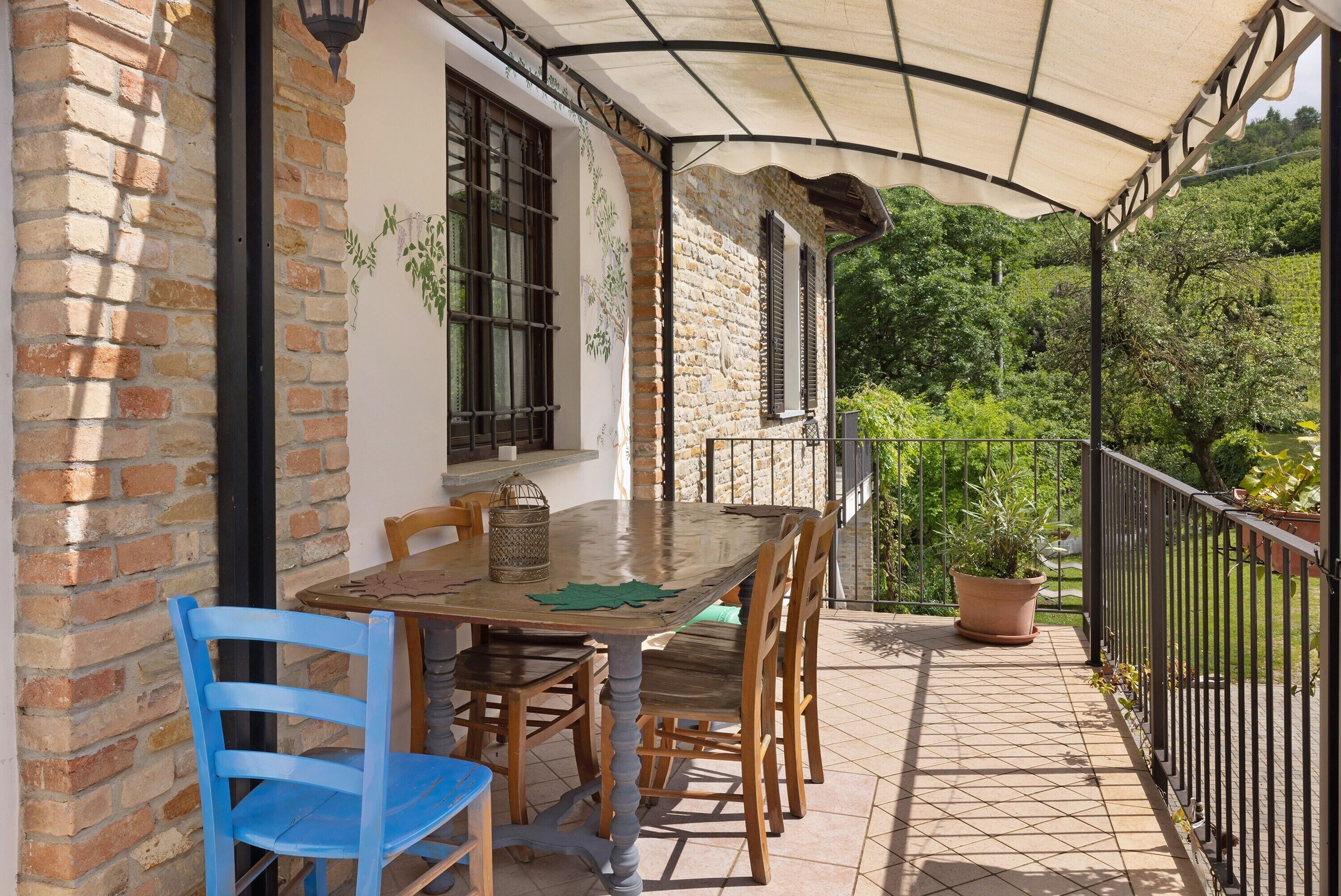 A covered outdoor patio with a table and chairs, a brick wall, and a view of greenery.