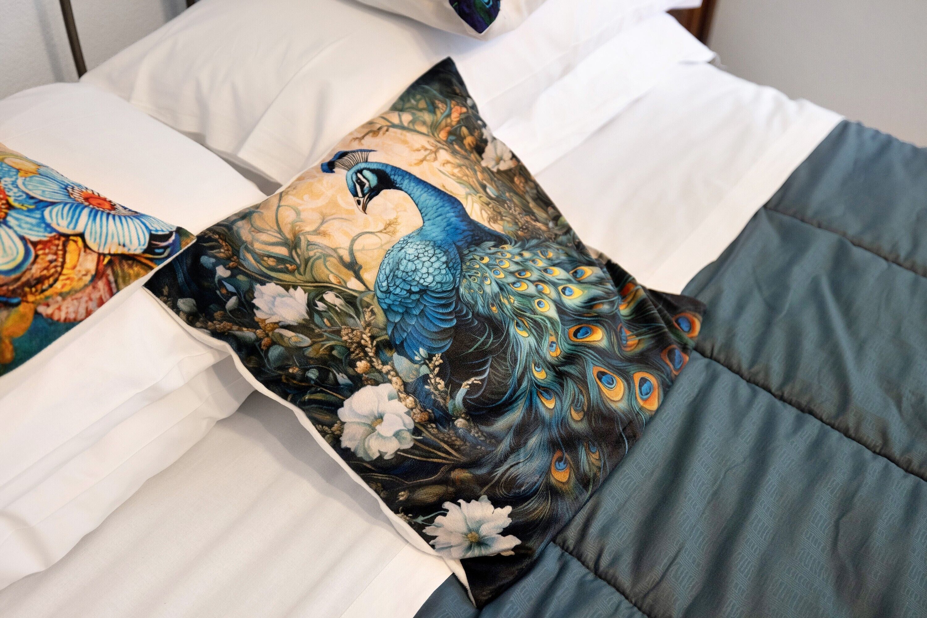Ein Bett mit blauer und weißer Bettwäsche, ein dekoratives Kissen mit Pfauenmuster und ein Blumenmuster auf dem Kissen.
