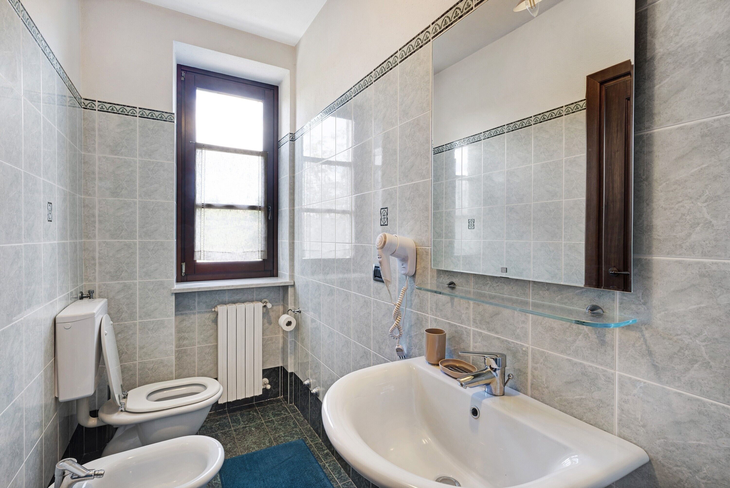 Un baño con inodoro, bidé, lavamanos y un estante de vidrio.
