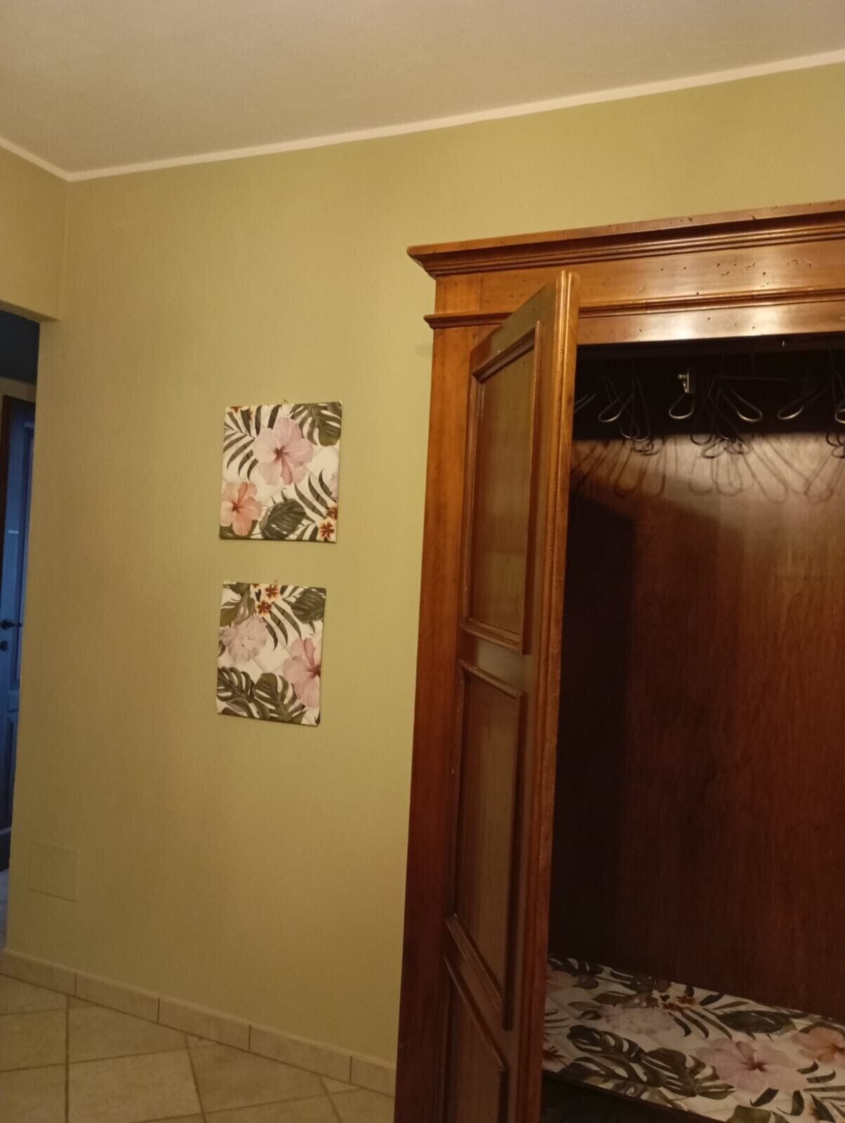 Una habitación con un armario de madera, piso de baldosas y dos cuadros de flores.