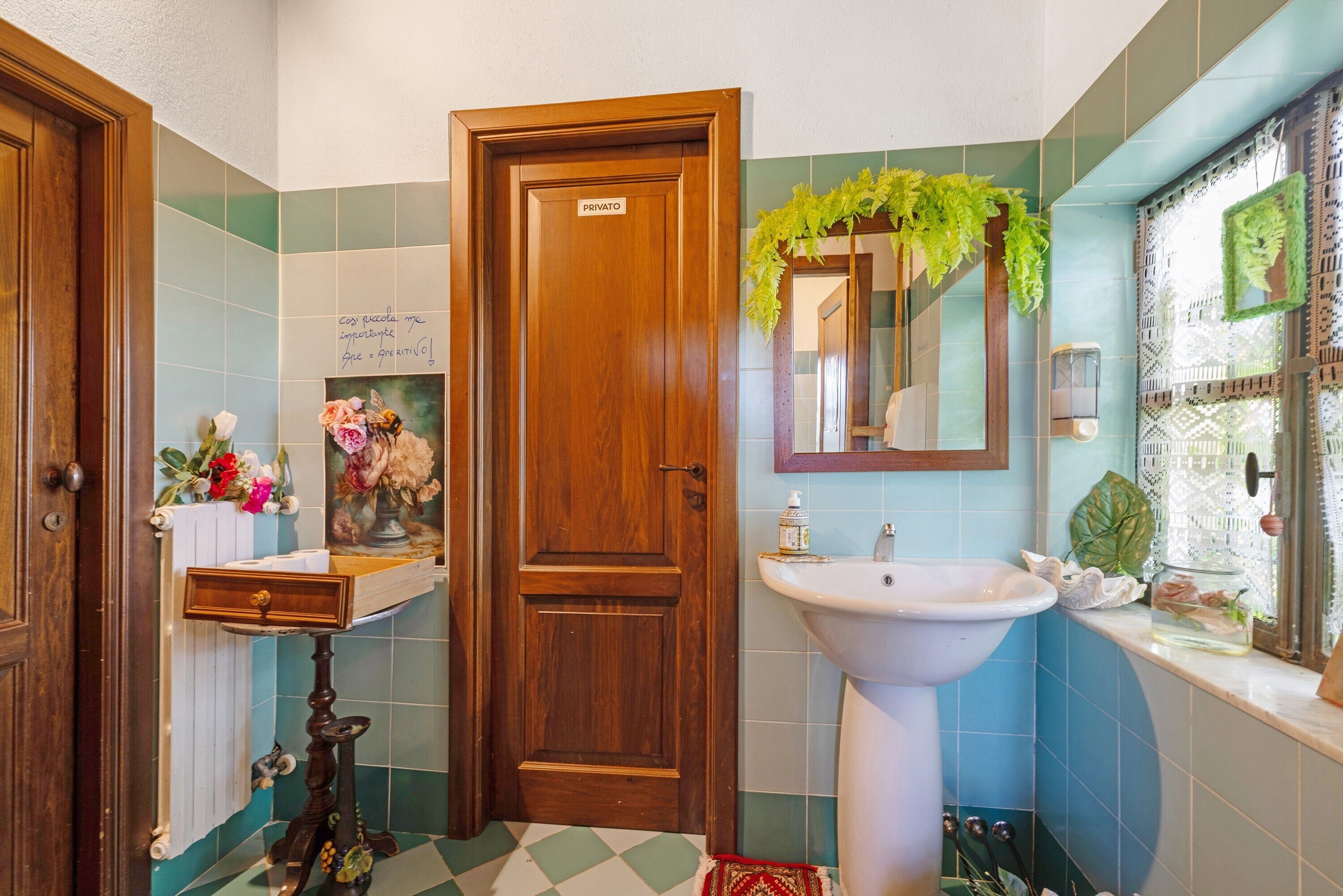 A bathroom with a wooden door, a sink, a mirror, and a tiled floor.