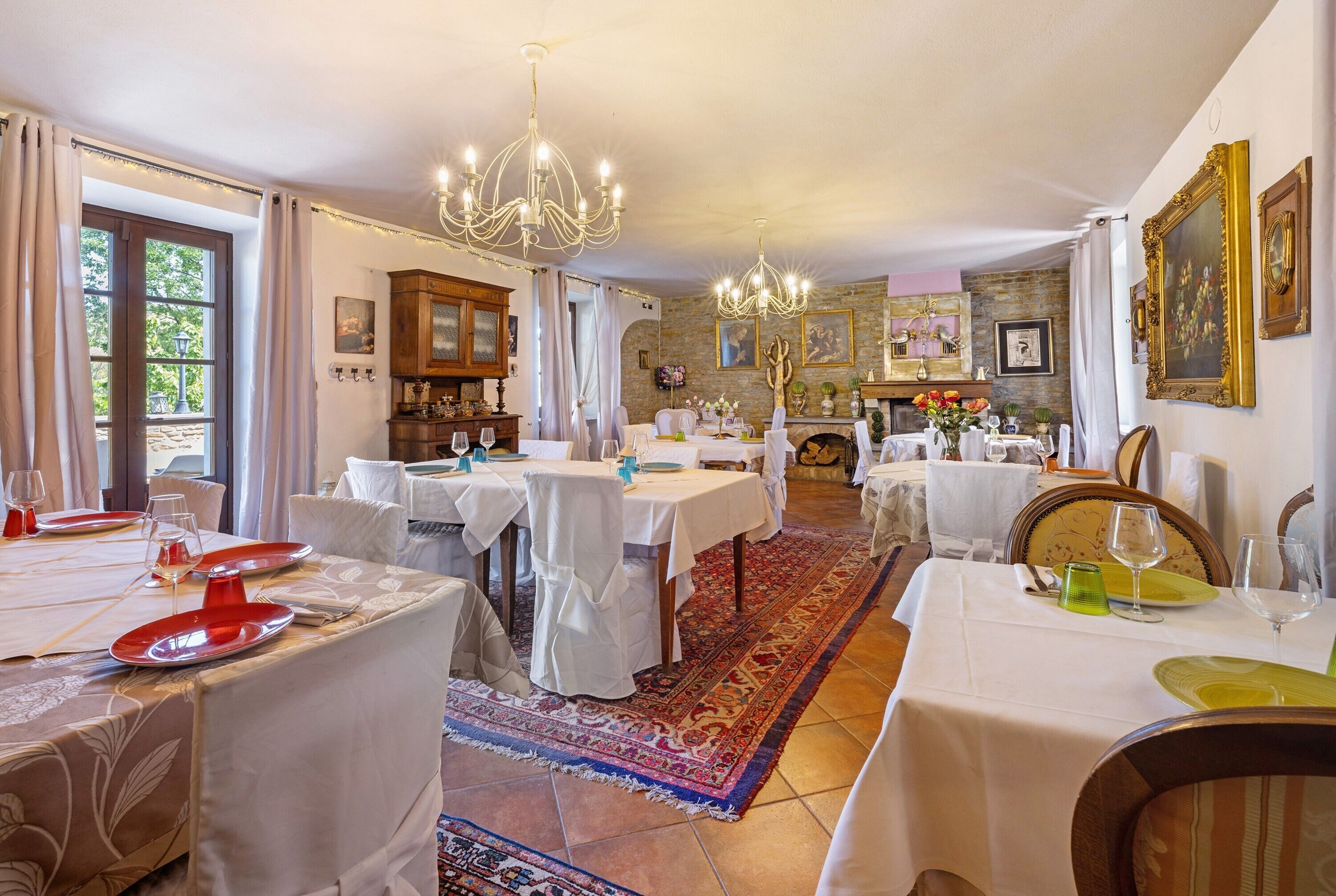 A dining area with multiple tables set for meals, a chandelier, and a view of the outdoors.