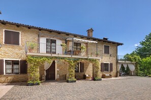 Un bâtiment en pierre doté d’un balcon, de plantes en pot et d’une cour dallée.