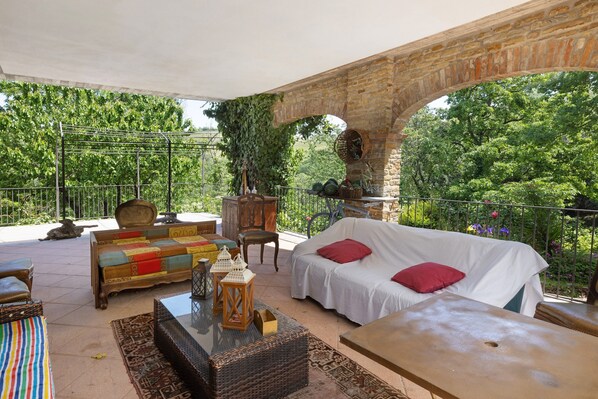 An outdoor patio with a stone arch, wicker furniture, and a white sofa with red cushions.