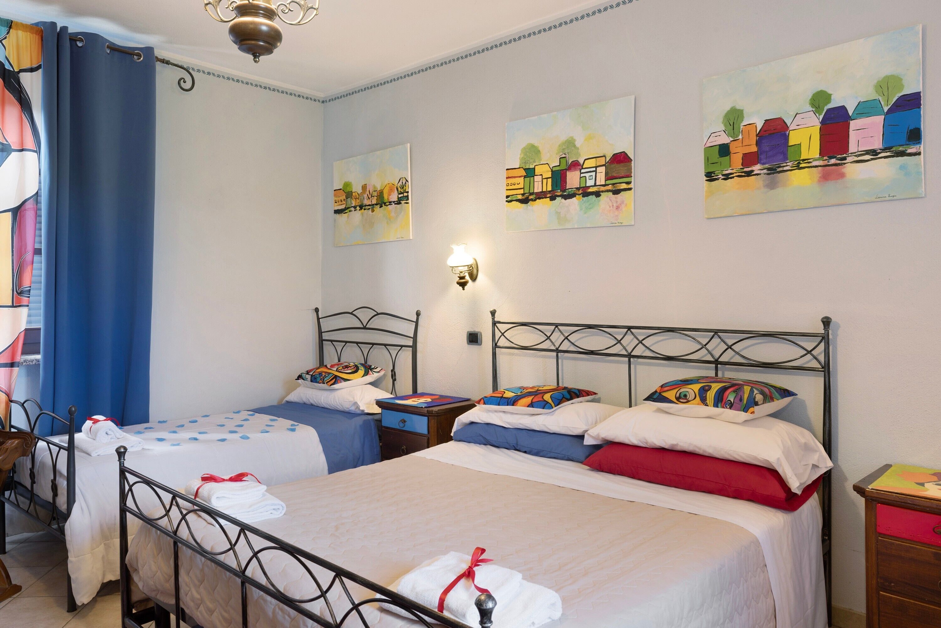 Una habitación de hotel con dos camas, una mesita de noche, una lámpara y obras de arte en las paredes.