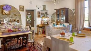 Un espace repas avec des tables dressées pour le repas, un lustre et un mur en pierre.