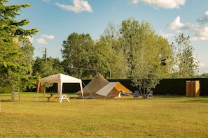A grassy outdoor area with a white tent, a yellow tent, and a picnic table.