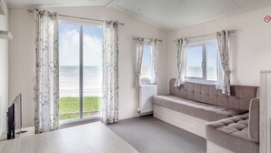 A room with a large window, a sofa, a table, and a radiator. - Castaways Oyster 8 Sea View (Pet) (Bacton-on-Sea)
