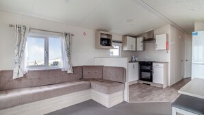 A compact living space with a sofa, kitchenette, and a window with curtains. - Castaways Oyster 8 Sea View (Pet) (Bacton-on-Sea)