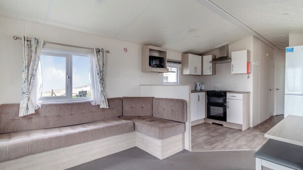 A compact living space with a sofa, kitchenette, and a window with curtains. - Castaways Oyster 8 Sea View (Pet) (Bacton-on-Sea)