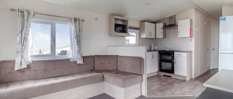 A compact living space with a sofa, kitchenette, and a window with curtains.