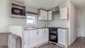 A compact kitchenette with a microwave, stove, sink, and cabinets. - Castaways Oyster 8 Sea View (Pet) (Bacton-on-Sea)