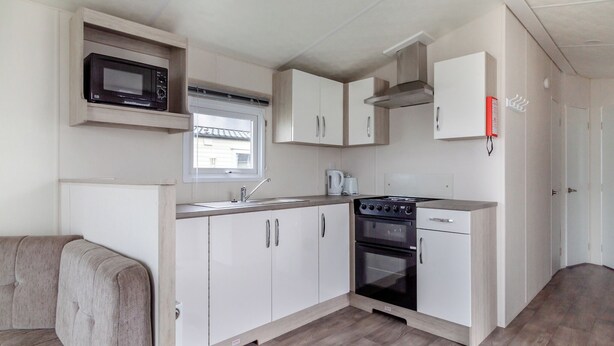 A compact kitchenette with a microwave, stove, sink, and cabinets. - Castaways Oyster 8 Sea View (Pet) (Bacton-on-Sea)