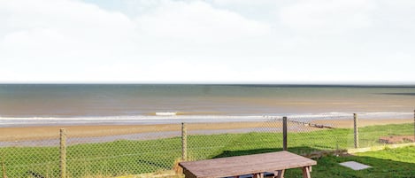 A picnic table and a chain-link fence overlooking a beach.