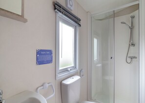 A bathroom with a toilet, a window, a shower, and a sign indicating a septic tank. - Castaways Oyster 8 Sea View (Pet) (Bacton-on-Sea)