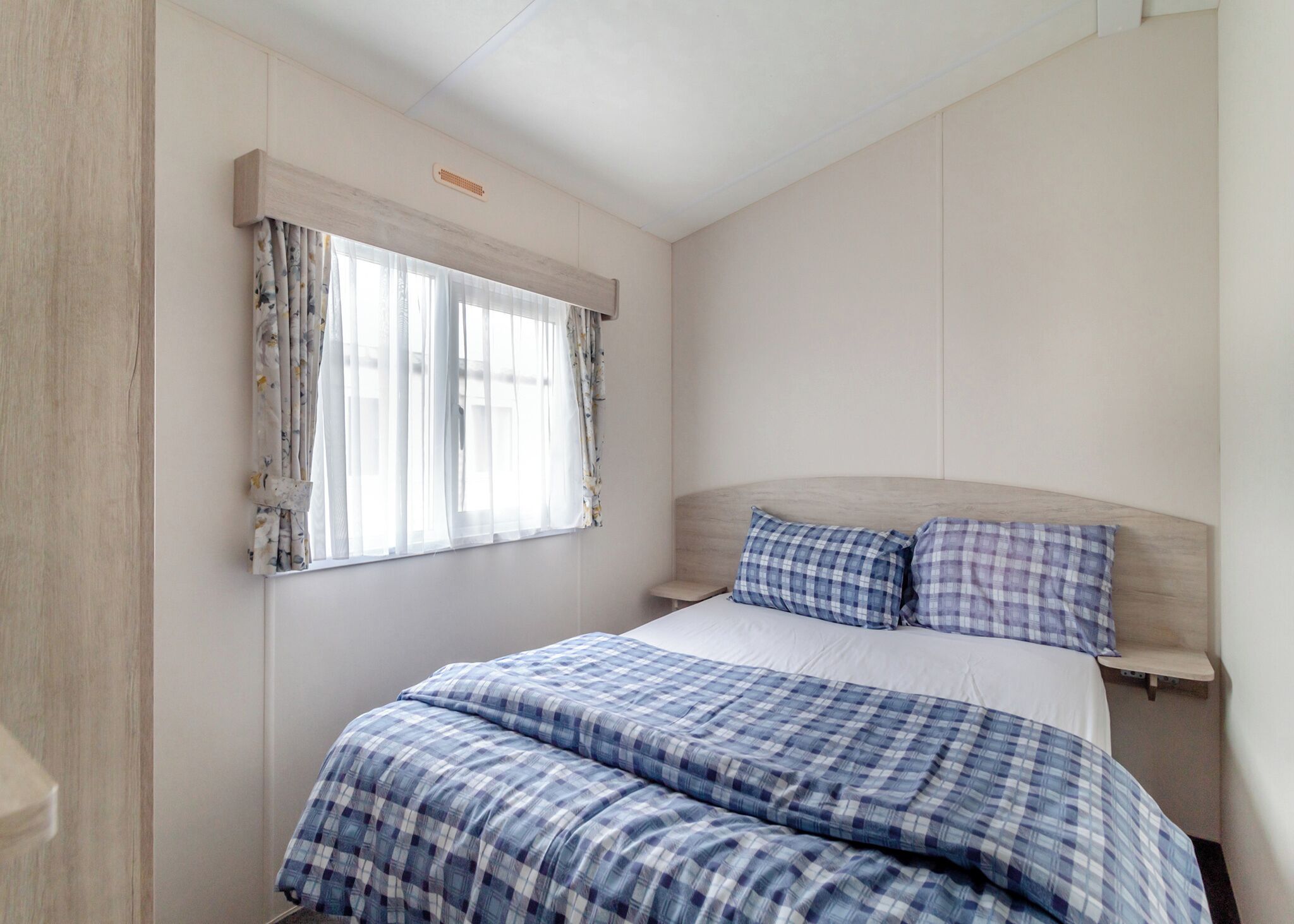 A bedroom with a bed, curtains, a headboard, and a bedside table.