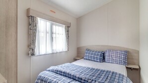 A bedroom with a bed, curtains, a headboard, and a bedside table. - Castaways Oyster 8 Sea View (Pet) (Bacton-on-Sea)