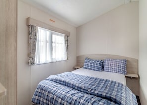 A bedroom with a bed, curtains, a headboard, and a bedside table.