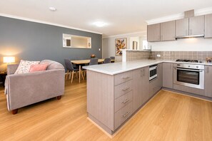 A modern kitchen with grey cabinets, a central island, and a dining area with a grey sofa and table.