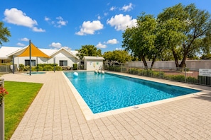 A rectangular swimming pool with a safety sign, surrounded by a paved walkway, a yellow canopy, and a white building with a metal roof. - Salty Sands (Broadwater)