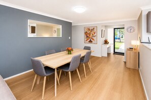 A modern dining area with a wooden table, grey chairs, and a vase of flowers. - Salty Sands (Broadwater)