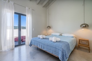 A bedroom with a bed, two bedside tables, a hanging lamp, and a sliding glass door to an outdoor area.