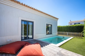 A modern house with a swimming pool, a wooden deck, and a fenced backyard.