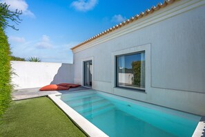 Una casa moderna con piscina, patio con cuscini e parete esterna bianca.
