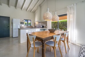 A modern kitchen with a wooden dining table, white chairs, and pendant lights.