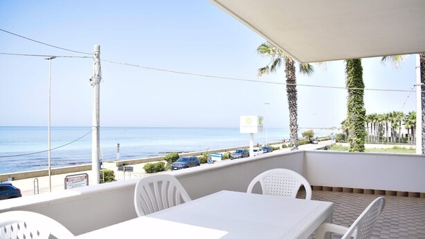 A balcony with a table and chairs, overlooking a beach and the sea.